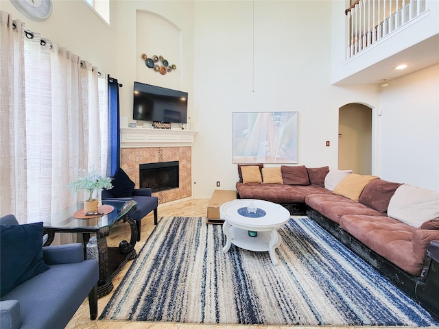 living room featuring arched walkways, a high ceiling, a healthy amount of sunlight, and a fireplace