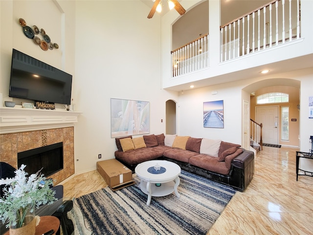 living room with stairs, marble finish floor, arched walkways, ceiling fan, and a towering ceiling