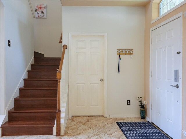 foyer with stairway, marble finish floor, and baseboards