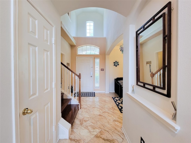 entrance foyer with marble finish floor, a towering ceiling, arched walkways, baseboards, and stairs
