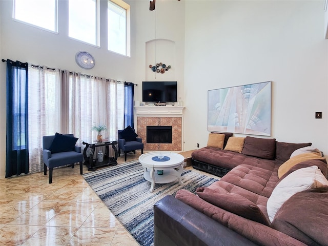 living room featuring marble finish floor, a high ceiling, a ceiling fan, and a tiled fireplace