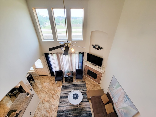 living room with a ceiling fan, a towering ceiling, and a fireplace
