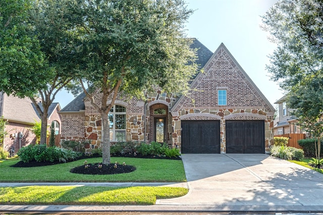 english style home with stone siding, concrete driveway, brick siding, a garage, and a front yard