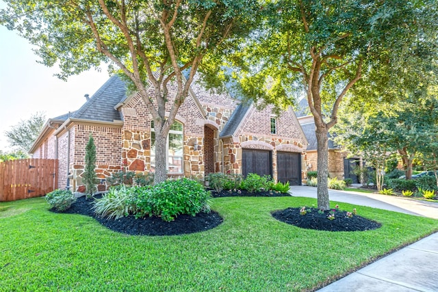 english style home with a gate, driveway, fence, a garage, and brick siding