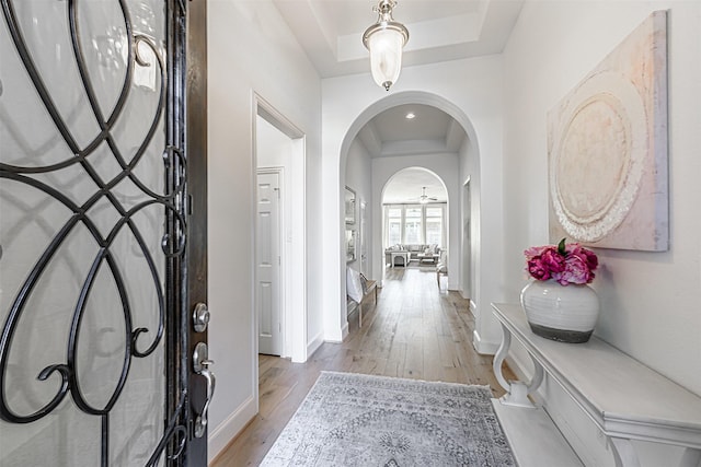 entryway featuring light wood finished floors, baseboards, a tray ceiling, and arched walkways