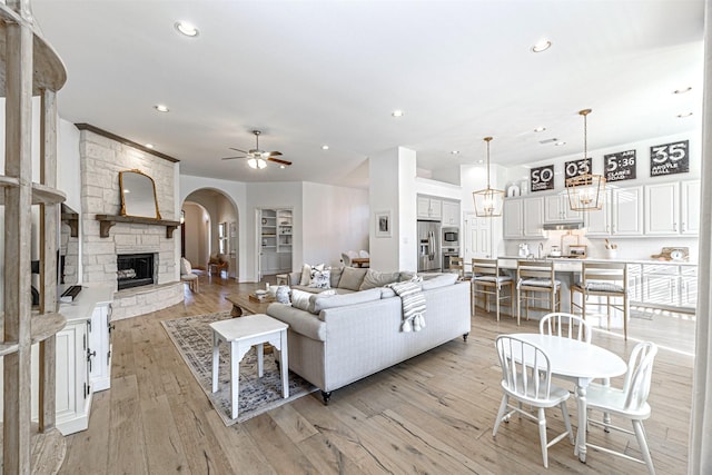 living room featuring recessed lighting, arched walkways, light wood-type flooring, a fireplace, and ceiling fan with notable chandelier