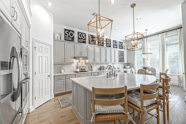 kitchen with light wood-style floors, a notable chandelier, light countertops, under cabinet range hood, and appliances with stainless steel finishes
