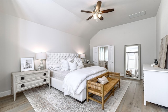 bedroom featuring light wood finished floors, vaulted ceiling, visible vents, connected bathroom, and baseboards