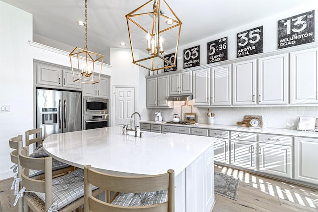 kitchen featuring a sink, backsplash, a notable chandelier, under cabinet range hood, and appliances with stainless steel finishes