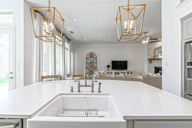 kitchen with recessed lighting, ceiling fan with notable chandelier, pendant lighting, light countertops, and a stone fireplace