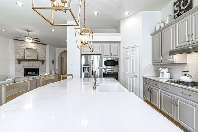 kitchen with ceiling fan with notable chandelier, appliances with stainless steel finishes, gray cabinets, and a sink