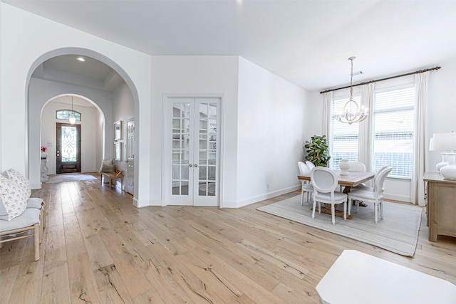 dining space with arched walkways, an inviting chandelier, french doors, light wood-style flooring, and baseboards