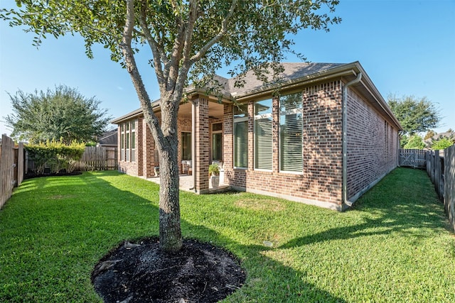 back of property with a fenced backyard, brick siding, a yard, and a patio