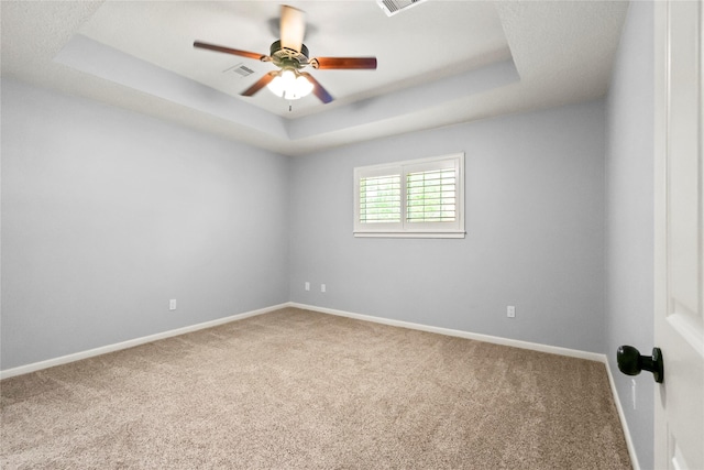 carpeted empty room featuring visible vents, baseboards, a raised ceiling, and a ceiling fan