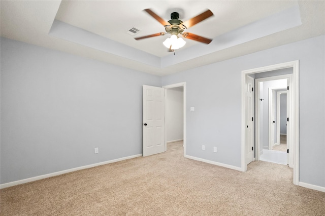 unfurnished bedroom featuring a tray ceiling, light colored carpet, baseboards, and visible vents