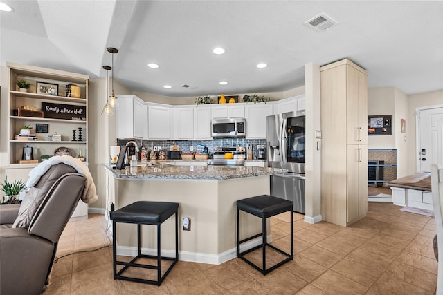 kitchen featuring light stone counters, a breakfast bar area, stainless steel appliances, a peninsula, and visible vents