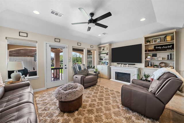 living area with visible vents, built in features, a ceiling fan, and a glass covered fireplace