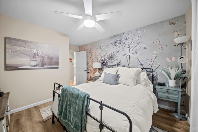 bedroom with wood finished floors, an accent wall, baseboards, and a ceiling fan