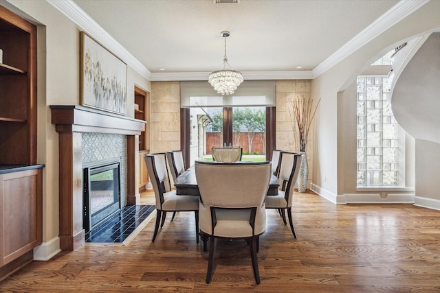 4404 Wendell St, Bellaire, TX 77401 - dining room featuring a chandelier, wood finished floors, a tiled fireplace, crown molding, and baseboards