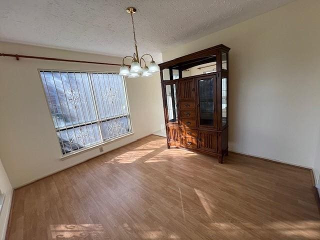 unfurnished dining area with a chandelier, a textured ceiling, and wood finished floors