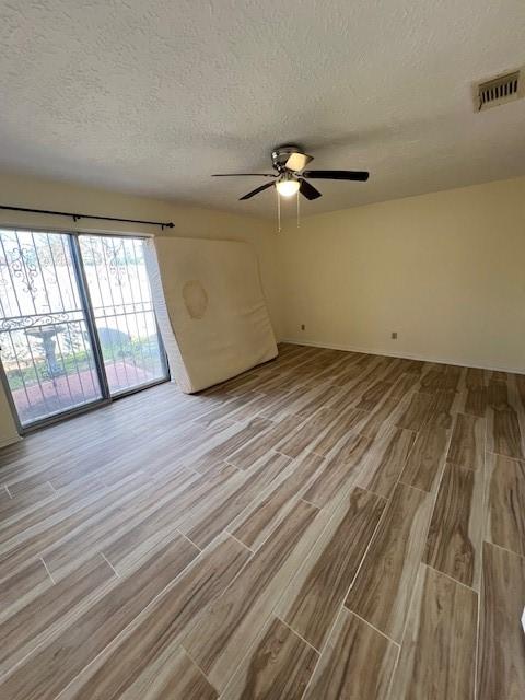 empty room with visible vents, a textured ceiling, a ceiling fan, and wood finished floors