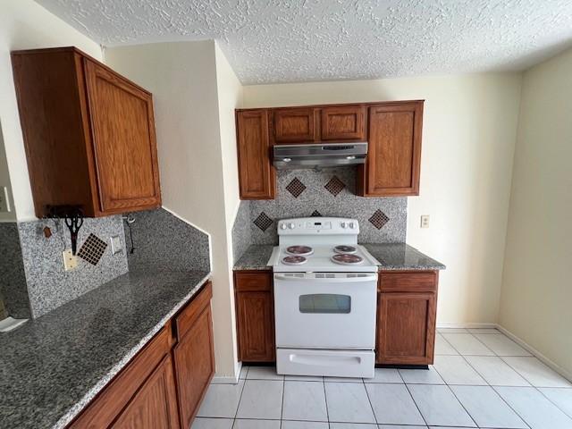 kitchen with dark stone counters, white range with electric cooktop, a textured ceiling, under cabinet range hood, and backsplash
