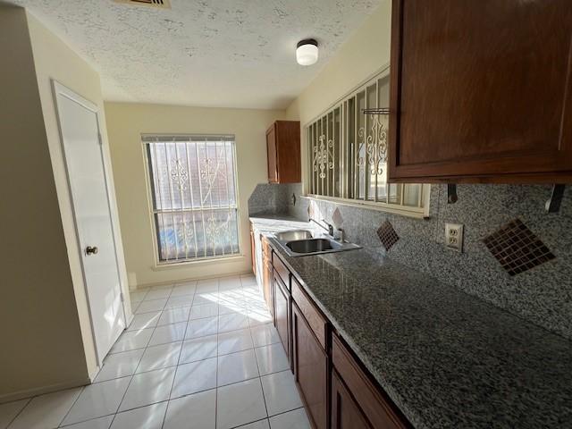kitchen with light tile patterned floors, tasteful backsplash, a textured ceiling, a sink, and baseboards