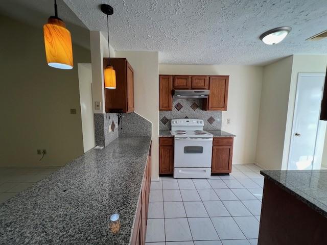 kitchen featuring tasteful backsplash, under cabinet range hood, white range with electric stovetop, light tile patterned flooring, and brown cabinets