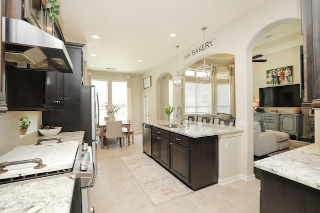 kitchen with arched walkways, a sink, a chandelier, under cabinet range hood, and appliances with stainless steel finishes