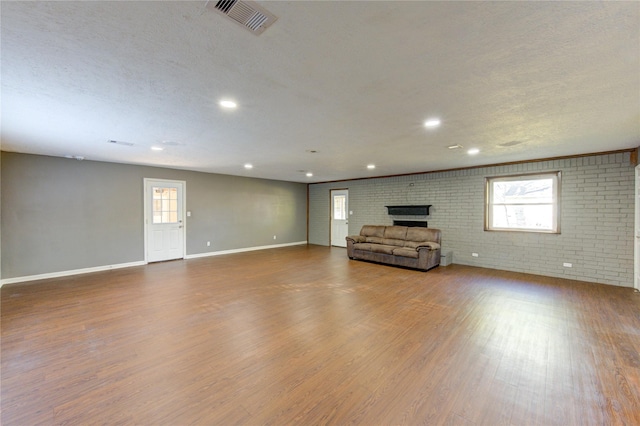 811 Strange Dr, Richmond, TX 77406 - unfurnished living room featuring brick wall, wood finished floors, visible vents, and plenty of natural light