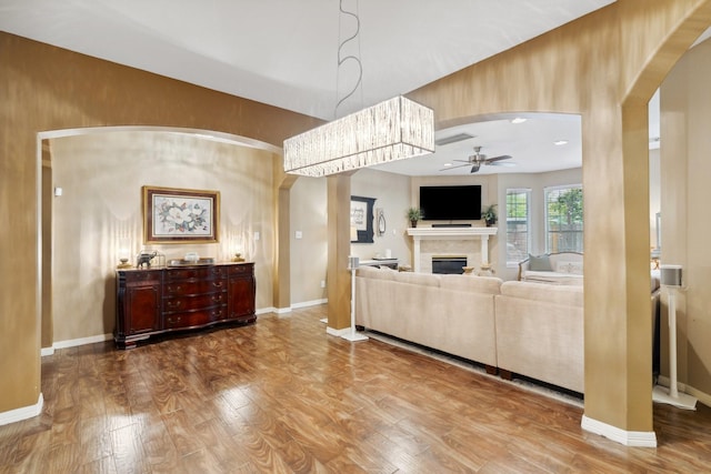 living area with arched walkways, a fireplace, dark wood-type flooring, and ceiling fan