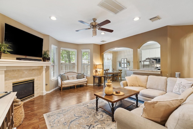 living room featuring arched walkways, ceiling fan, a fireplace, and visible vents