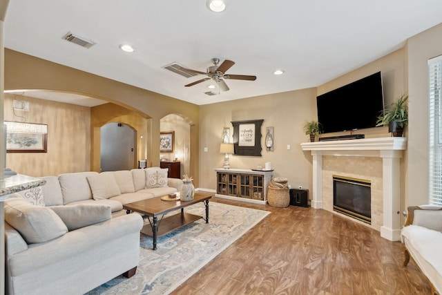 living area featuring visible vents, arched walkways, ceiling fan, wood finished floors, and a tile fireplace
