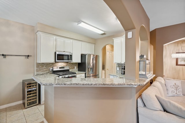 kitchen with tasteful backsplash, light stone countertops, appliances with stainless steel finishes, arched walkways, and beverage cooler