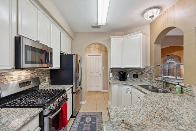 kitchen with arched walkways, white cabinetry, visible vents, a sink, and stainless steel appliances