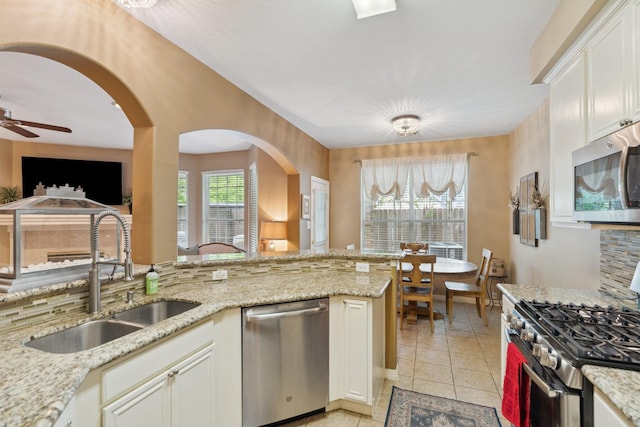 kitchen with light stone counters, ceiling fan, stainless steel appliances, arched walkways, and a sink