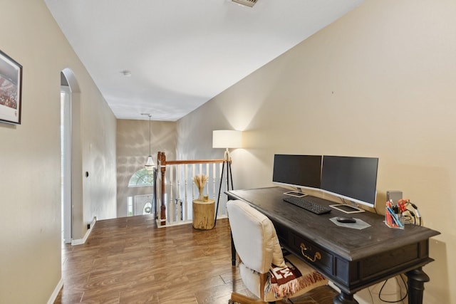 office area with arched walkways, baseboards, and wood finished floors