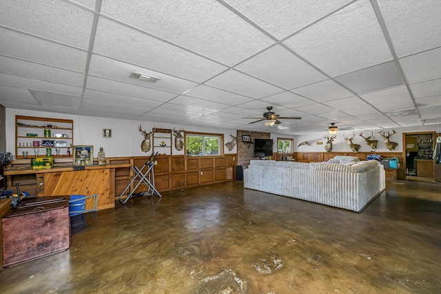 living room with visible vents, a ceiling fan, a drop ceiling, and finished concrete flooring