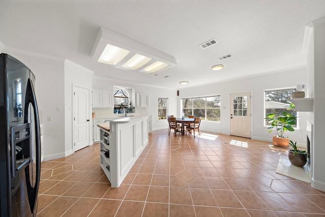 kitchen with light tile patterned floors, ornamental molding, visible vents, black refrigerator with ice dispenser, and light countertops