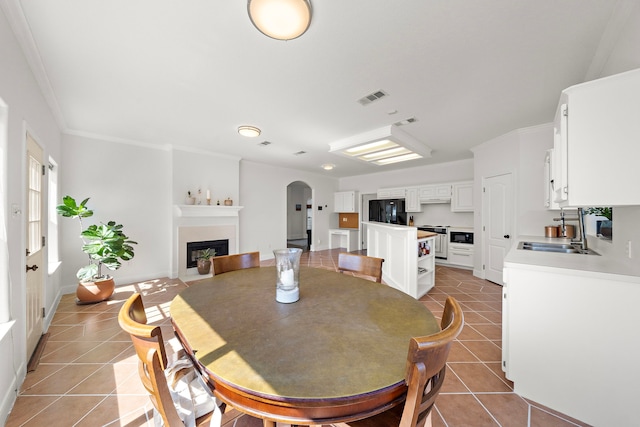 dining room featuring light tile patterned floors, arched walkways, visible vents, and a fireplace with flush hearth