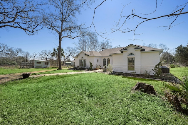 back of property featuring stucco siding, an outdoor structure, and a lawn