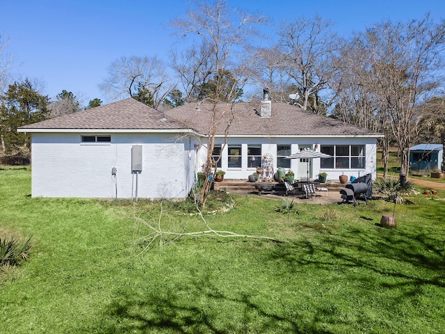 rear view of property featuring a yard, entry steps, a patio area, a chimney, and brick siding