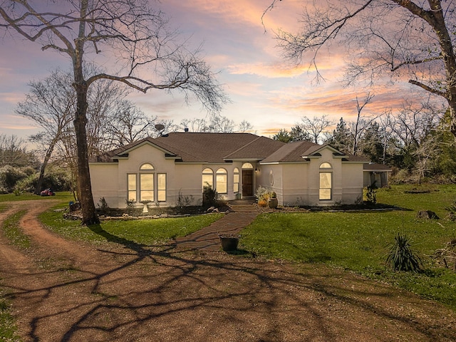 ranch-style house featuring stucco siding and a lawn