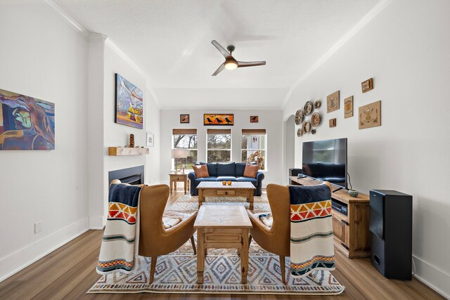 living room featuring crown molding, a fireplace, light wood-type flooring, a ceiling fan, and baseboards