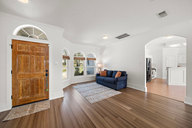 entryway with arched walkways, crown molding, and visible vents