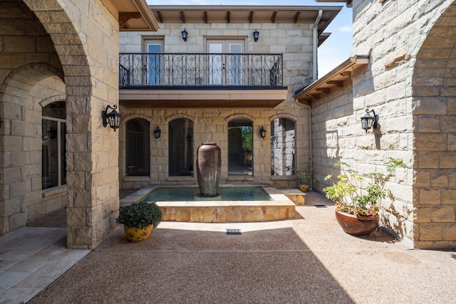 view of exterior entry with french doors, stone siding, and a balcony