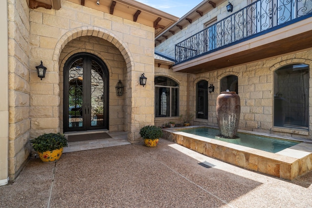 doorway to property with a balcony, french doors, and stone siding
