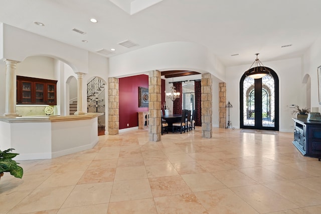 foyer entrance featuring french doors, visible vents, ornate columns, and a notable chandelier