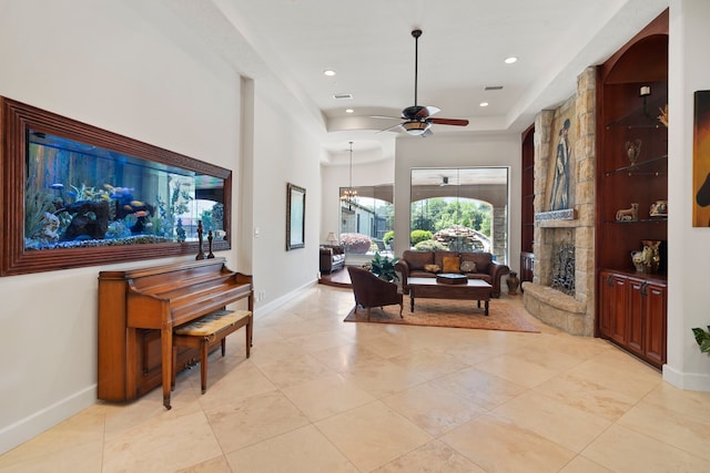 living room featuring a stone fireplace, baseboards, light tile patterned flooring, and ceiling fan with notable chandelier