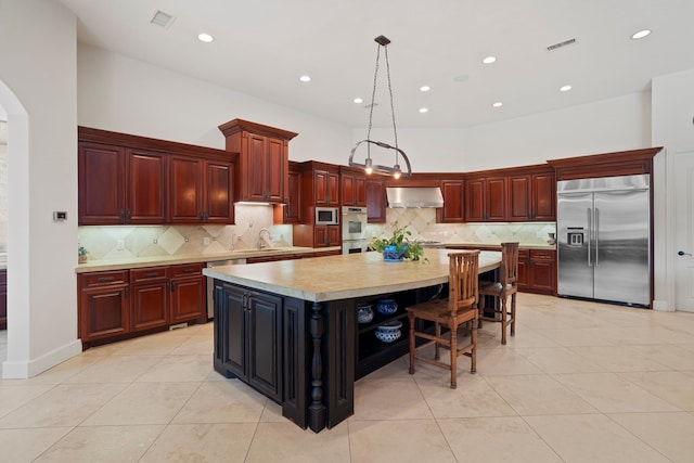 kitchen with wall chimney exhaust hood, visible vents, light countertops, a sink, and built in appliances